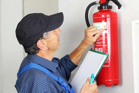 A man wearing blue jumper suit checking fire extinguisher with compliance